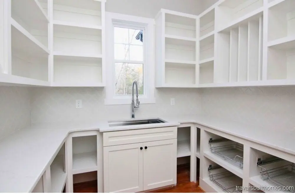 A scullery pantry with open white shelving, a second sink and a window